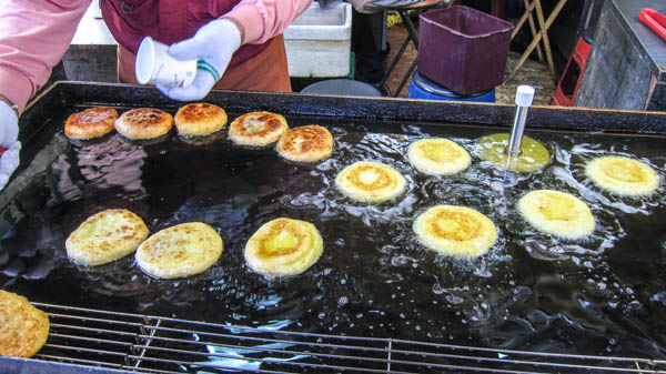 Hotteok being cooked in oil on a hot girdle
