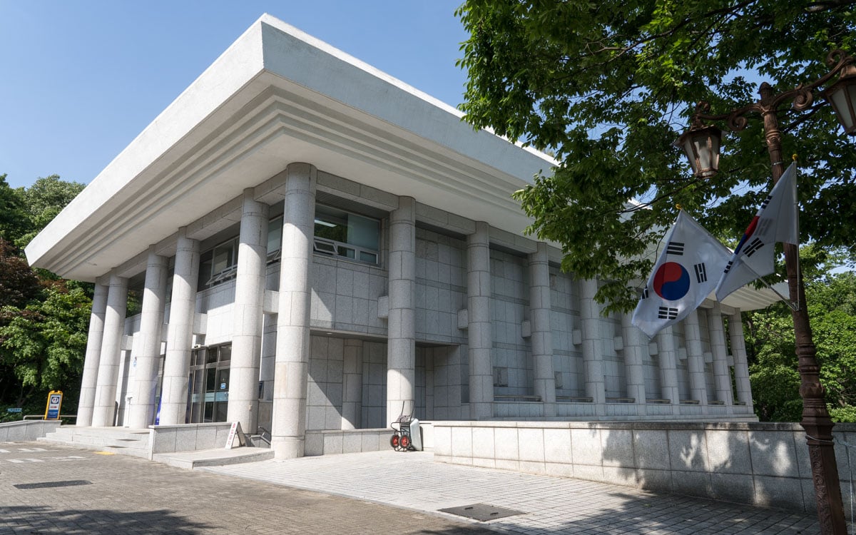 April 19th Revolution Memorial Hall, a white stone building with columns, shown beside trees and South Korean flags.